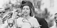 Rosa Parks speaks at a podium outside as people stand behind her