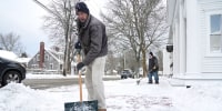 People shovel snow off of a sidewalk